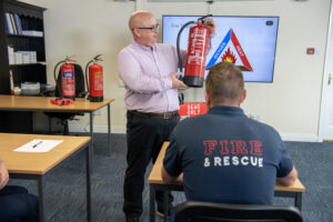 Ross Gernon demonstrating how to use a fire extinguisher to an attendee in the class